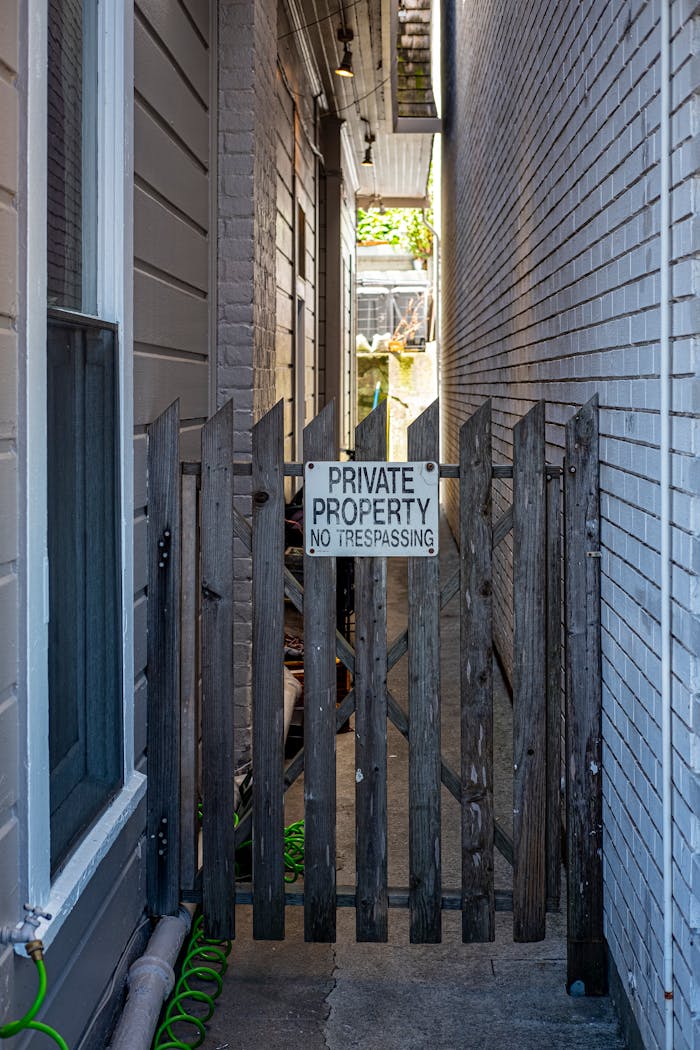 Vertical shot of a narrow private property entrance with a wooden gate and warning sign, no trespassing.